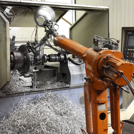 Roboterarm entnimmt einen PAR-64 Lampendeckel aus einer Drehbank